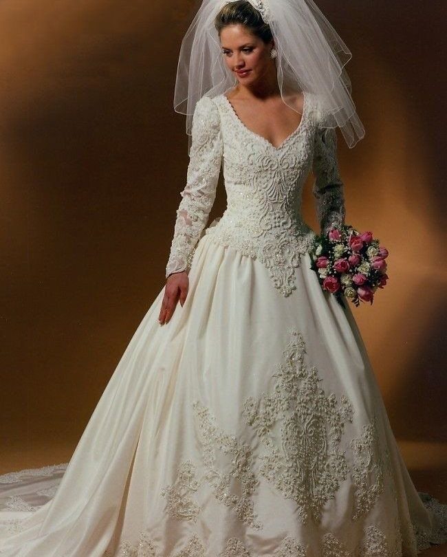 Woman in a white lace wedding dress with a veil holding pink roses.