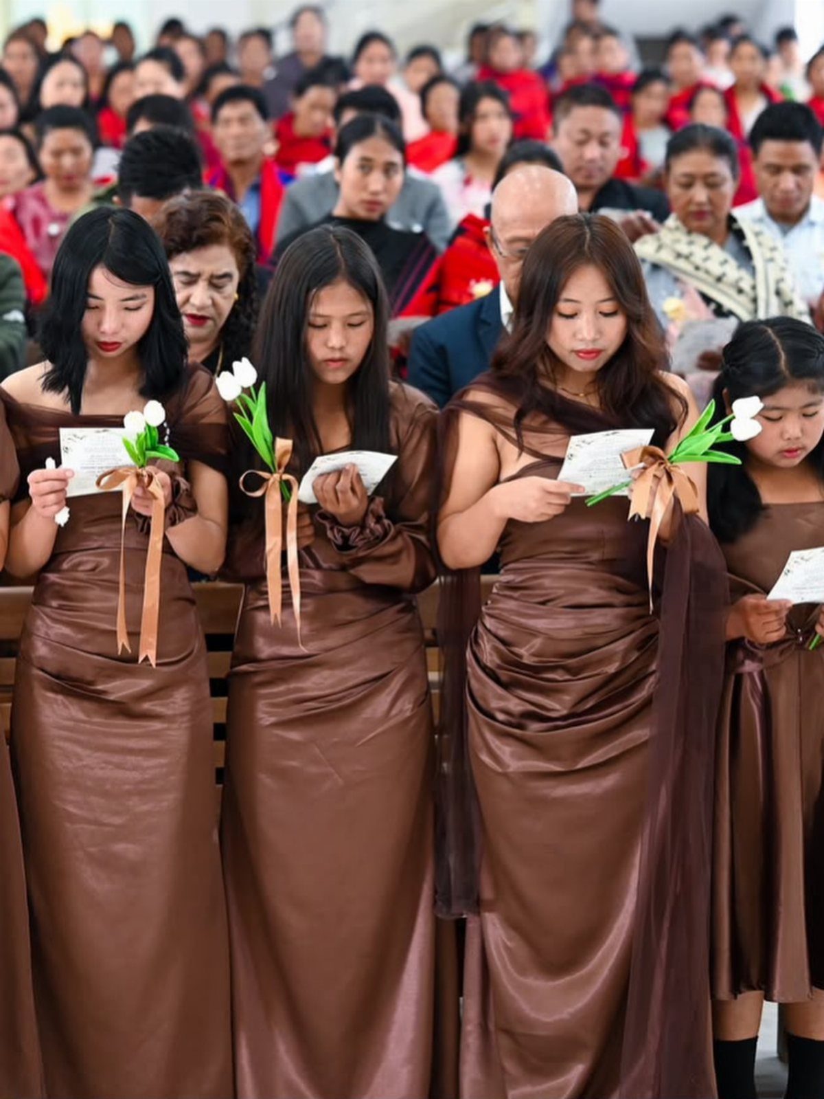 Four women in long brown satin bridesmaids dresses holding white tulips and cards.