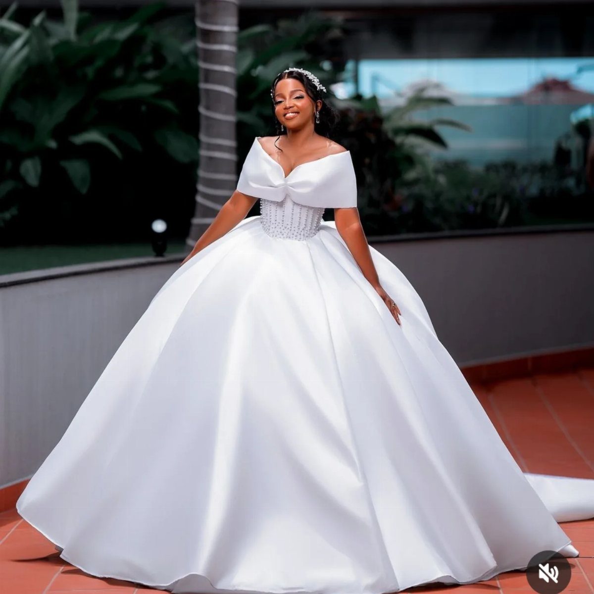 Woman in a voluminous white satin ballroom wedding gown posing outdoors on terracotta tiles.