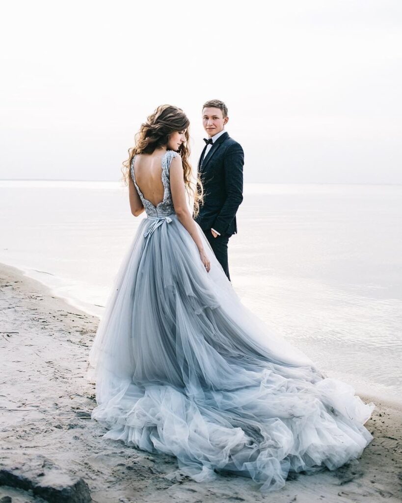 Woman in a flowing light blue wedding dress standing on a beach with groom.
