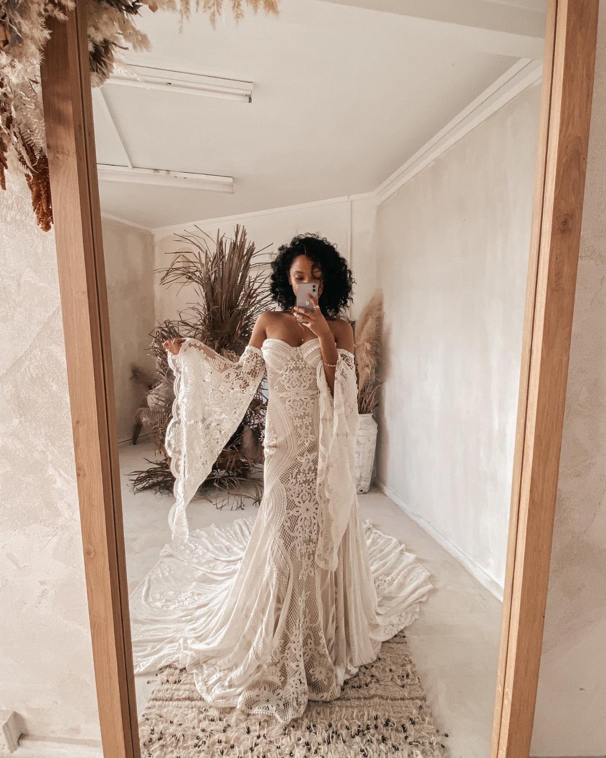 Woman in a white lace boho bridal gown with bell sleeves taking a selfie.
