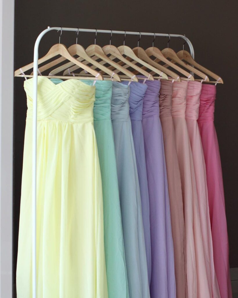Pastel bridesmaid dresses in fruity sorbet tones hanging on a white garment rack.