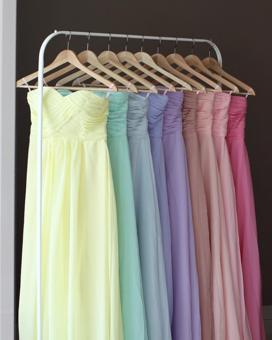 Pastel bridesmaid dresses in fruity sorbet tones hanging on a white garment rack.