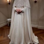 Woman wearing a white wedding dress with a beaded lace cape and long train.
