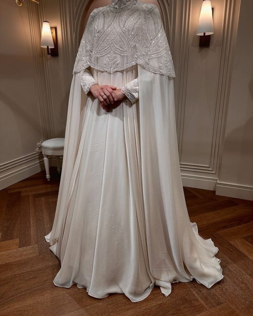 Woman wearing a white wedding dress with a beaded lace cape and long train.