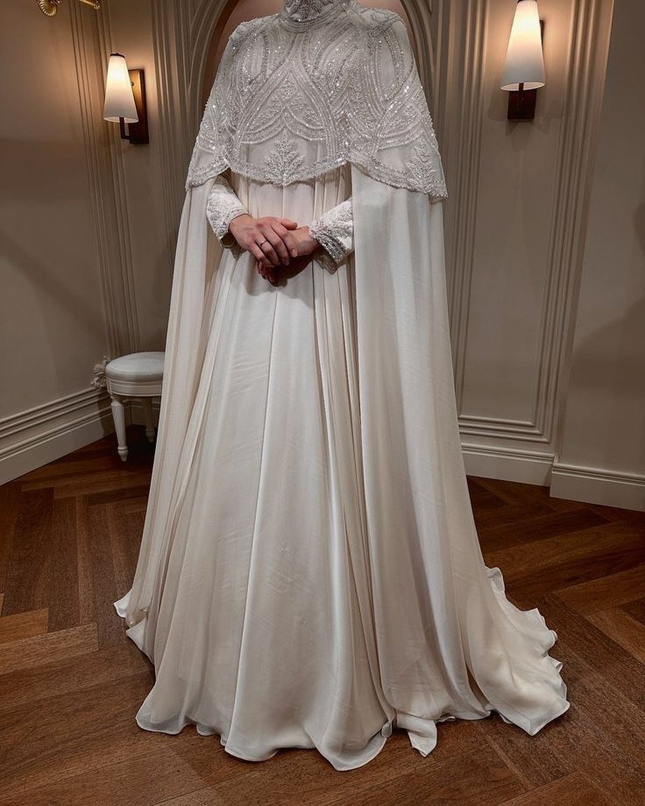 Woman wearing a white wedding dress with a beaded lace cape and long train.