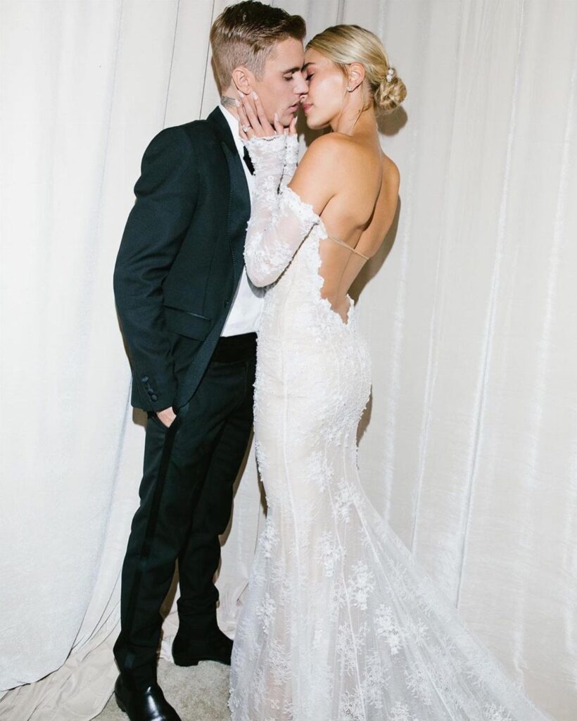 Hailey Bieber and Justin Bieber kissing, featuring her off-the-shoulder lace wedding dress.