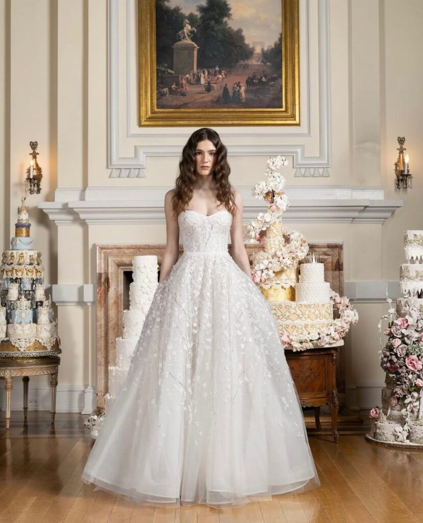 Woman in a strapless white beaded bridal gown standing among tiered wedding cakes.