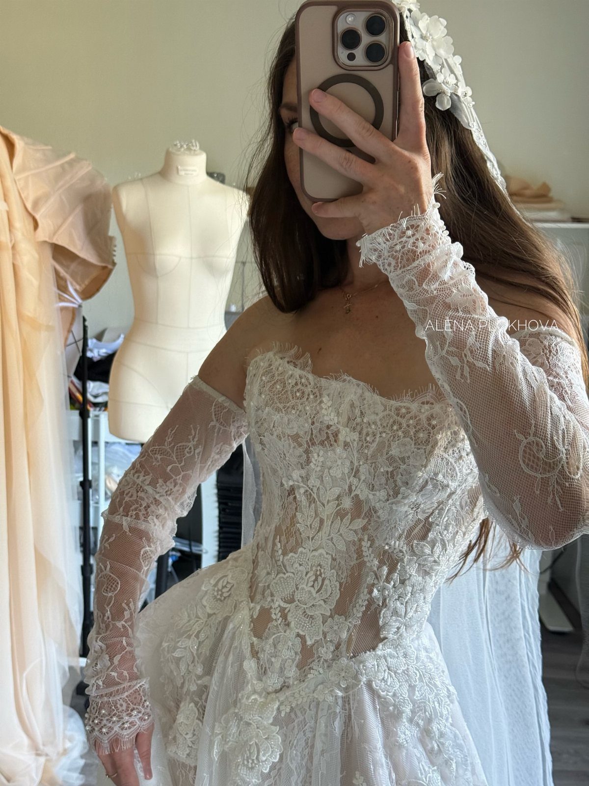 Woman in a white lace wedding dress with long sleeves taking a mirror selfie