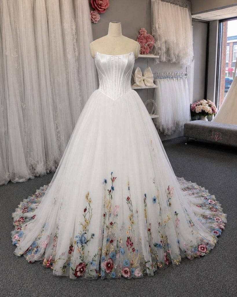 White strapless wedding dress on a mannequin with colorful floral embroidery on the skirt.