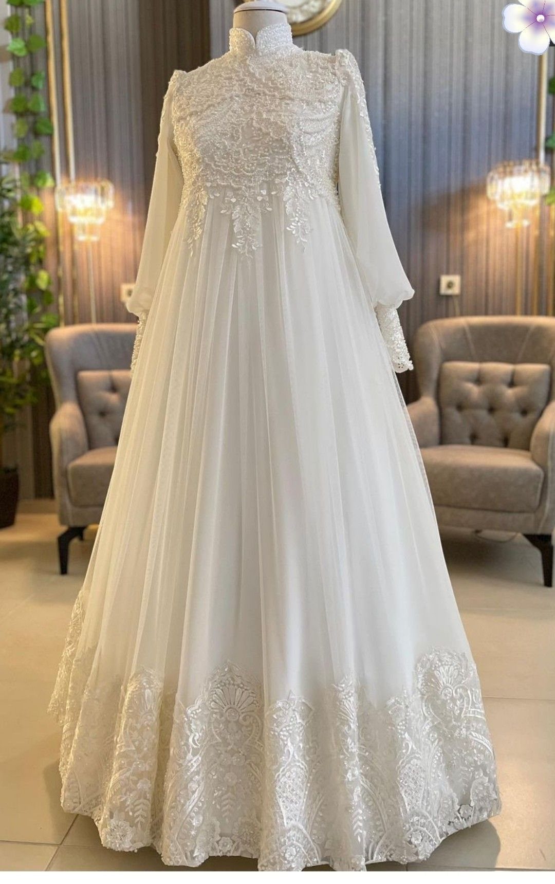 White long-sleeved wedding gown with lace embroidery on a mannequin in a room.