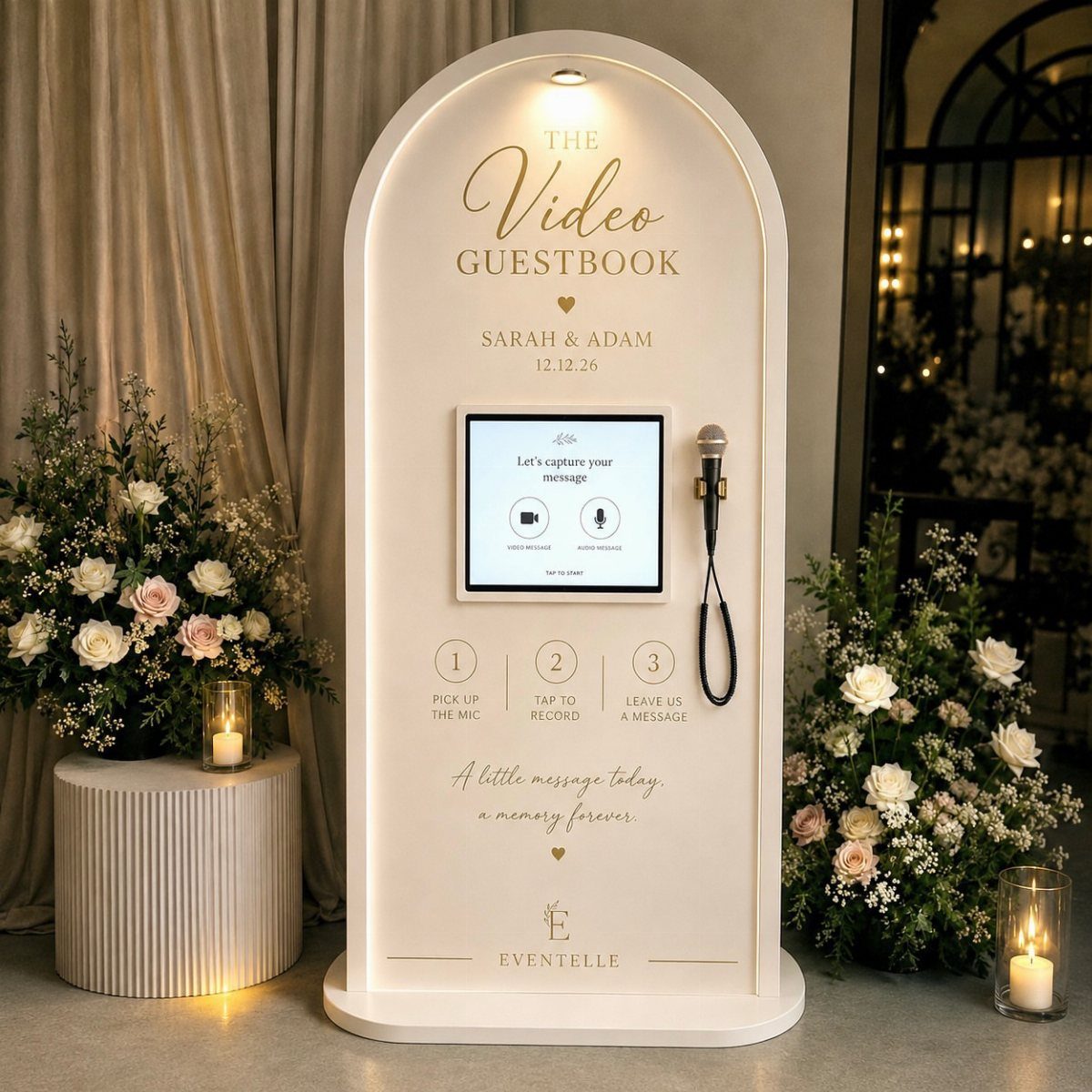 White arched video guestbook kiosk with flowers and candles at a wedding reception.