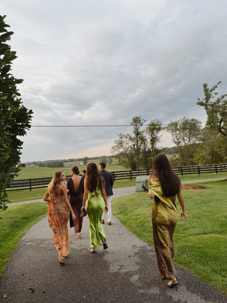 Four people in formal attire walking down a path in a countryside setting.