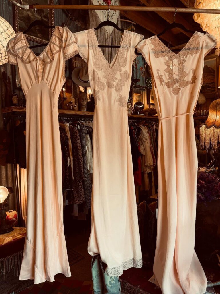 Three cream vintage wedding dresses hanging on a rack in a boutique store