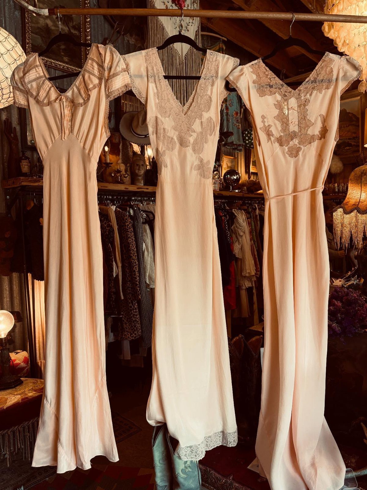 Three cream vintage wedding dresses hanging on a rack in a boutique store