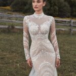 Woman in a white long-sleeved wedding dress with lace overlays in a field