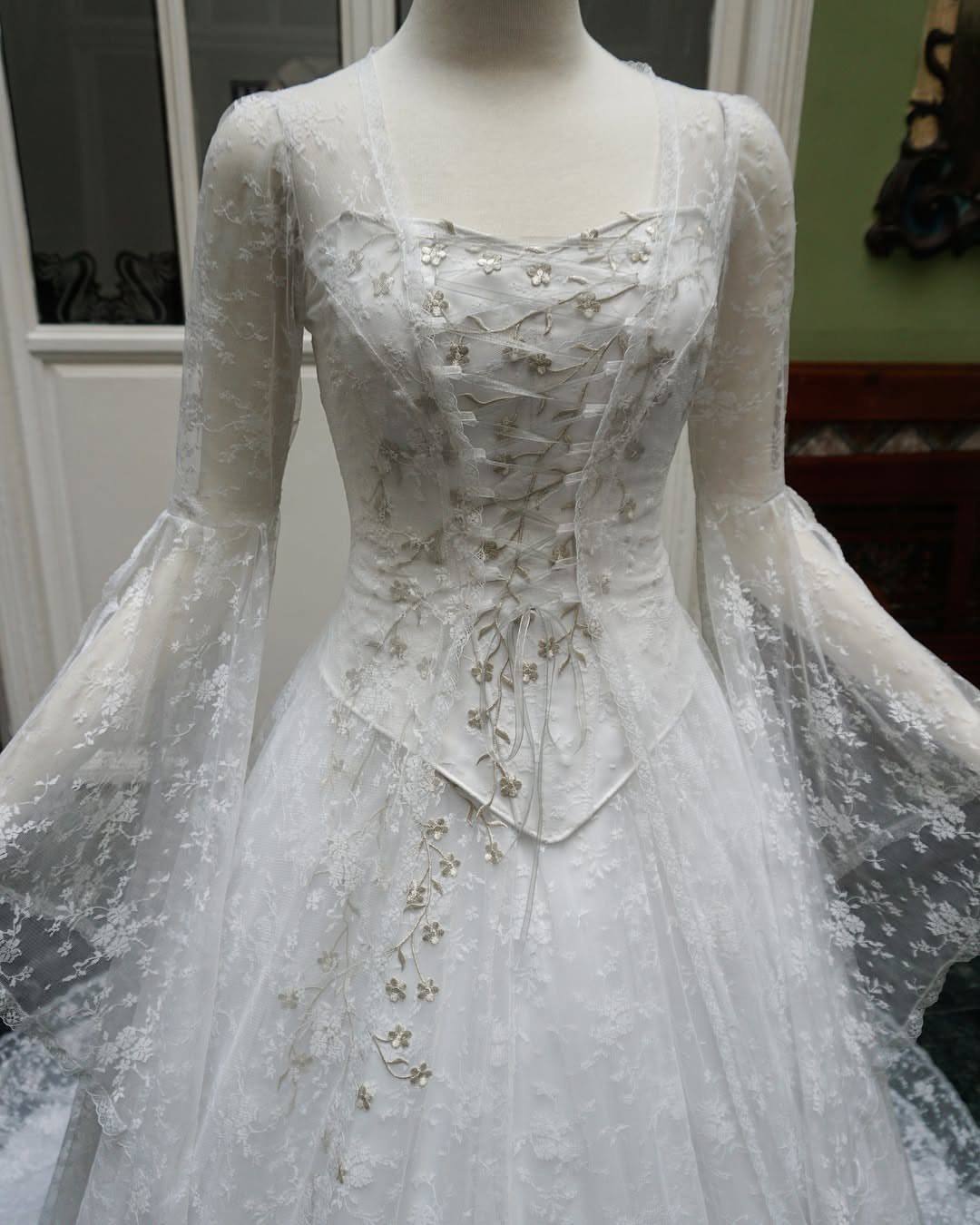 White lace medieval style wedding dress with bell sleeves on a mannequin