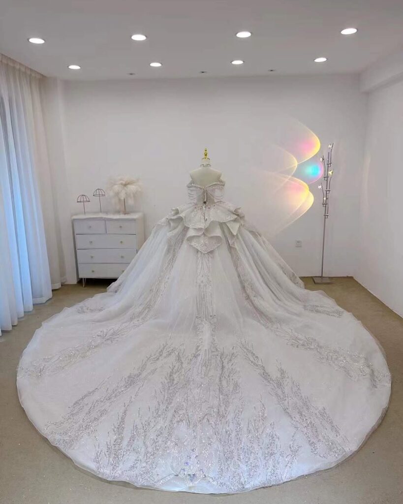 Ornate white wedding dress with a wide embroidered train on a mannequin.