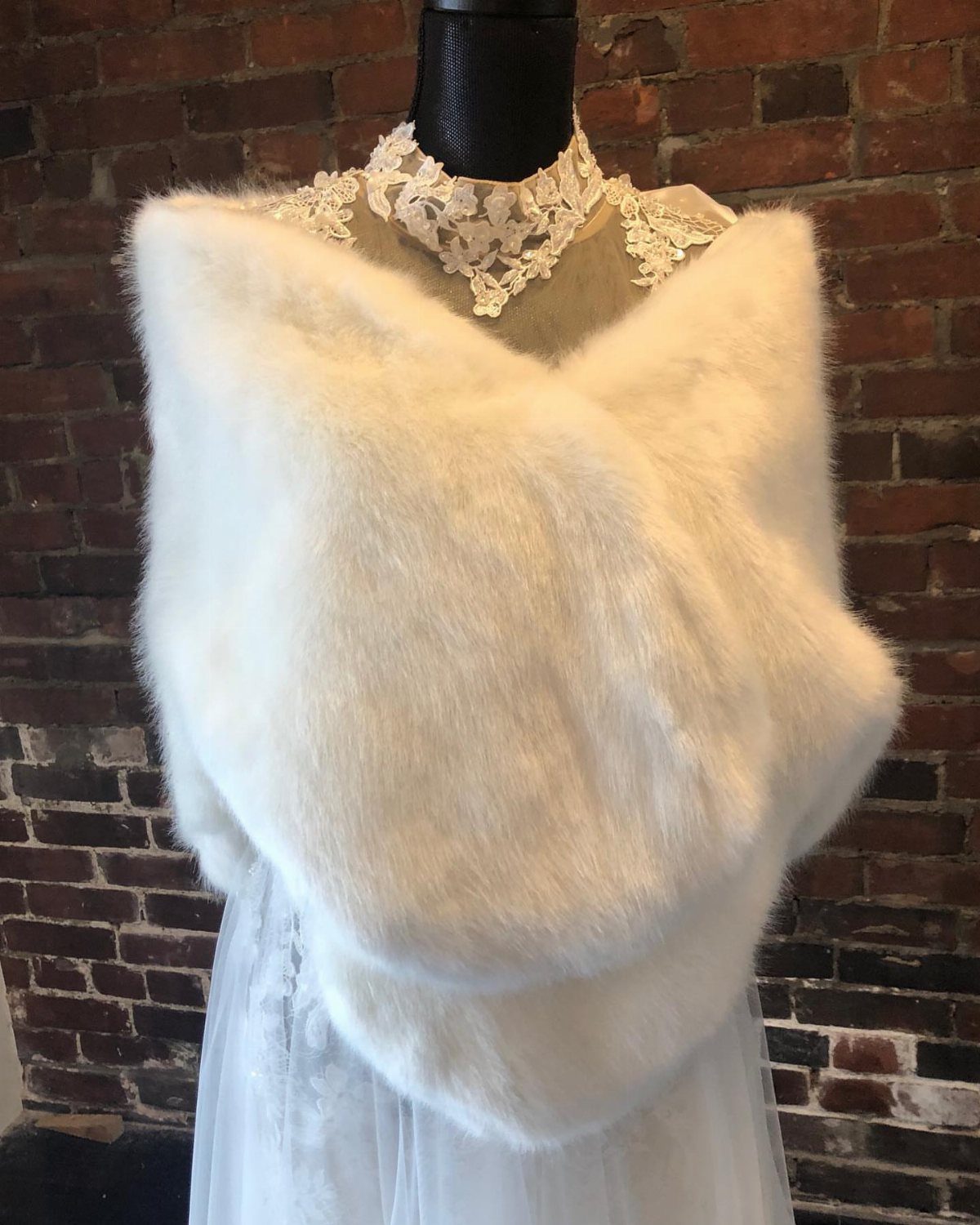 White faux-fur shawl draped over a lace wedding dress on a mannequin.