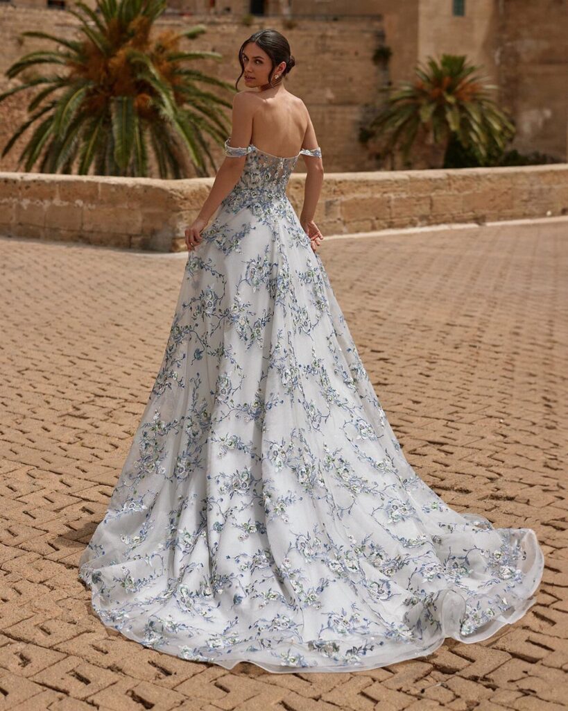 Woman in a white wedding gown with light blue floral embroidery on cobblestones