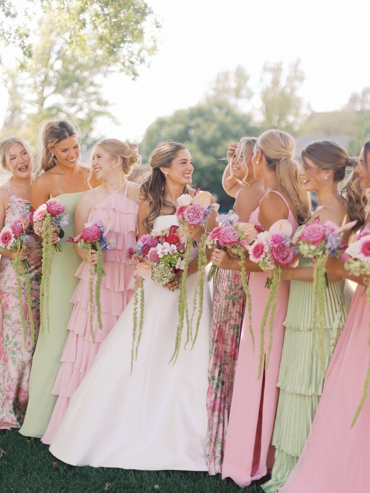 Bride in white dress and bridesmaids in pastel gowns holding colorful floral bouquets