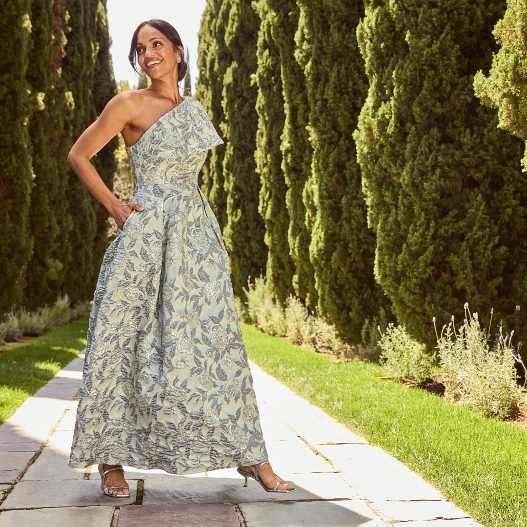 Woman in a floral one-shoulder maxi dress standing on a sunny garden path