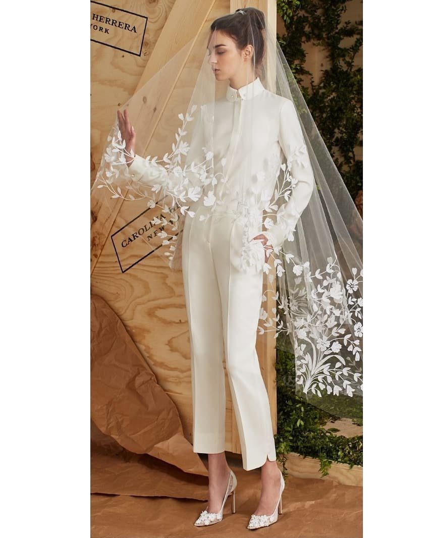 Woman in a white bridal suit and floral lace veil posing by wood.