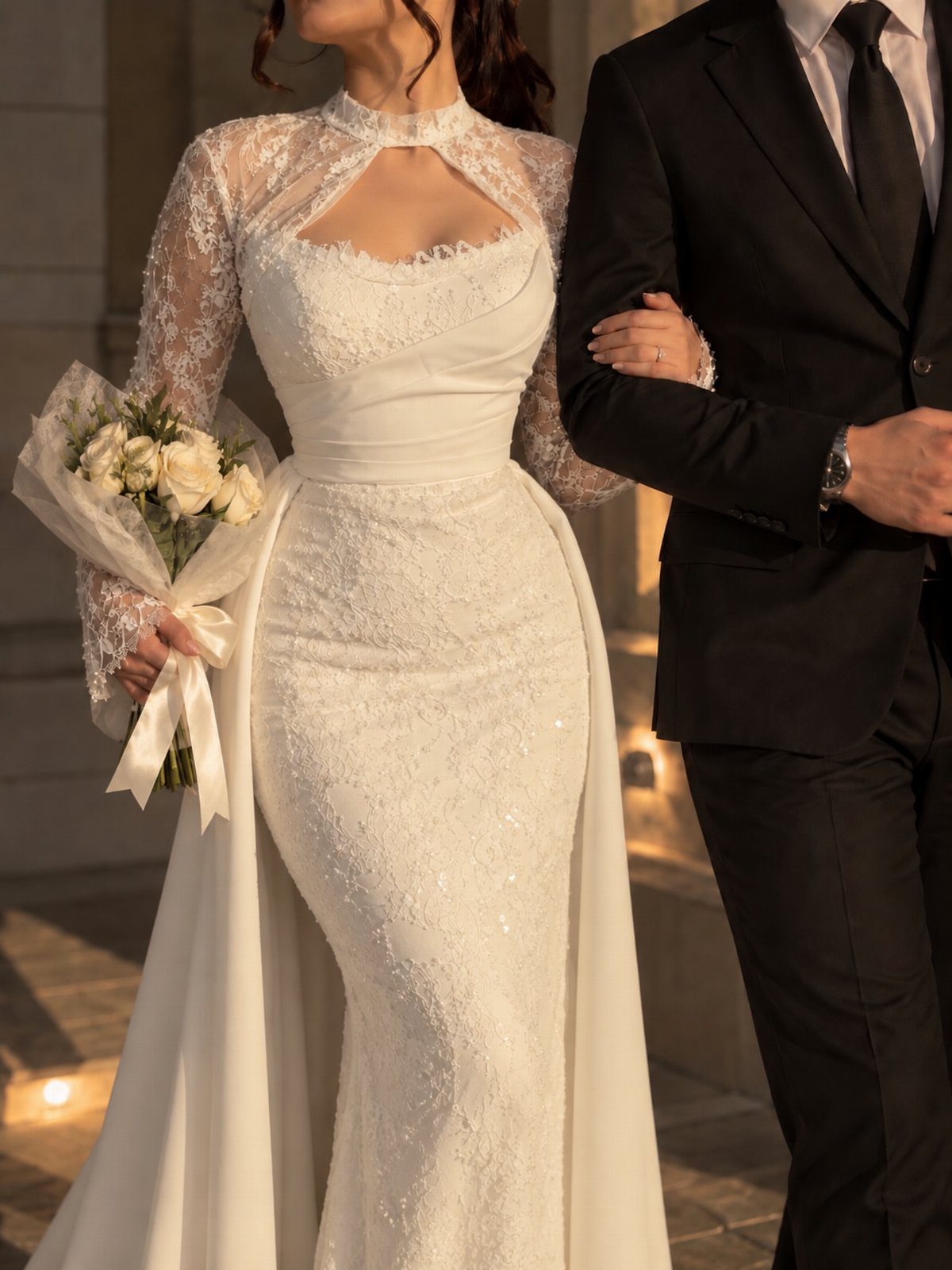 Woman in a white lace wedding dress with a cape holding white roses